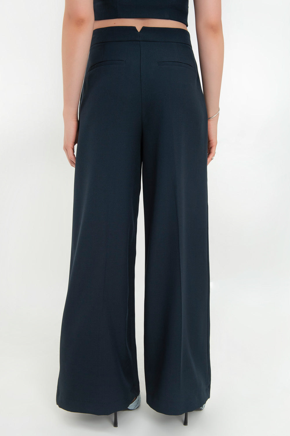 Pantalón de fit wide leg, cintura alta con pretina, pinzas frontales, bolsillos delanteros y vivos decorativos posteriores. Cierre frontal con broche y cremallera ocultos. Detalle v en pretina posterior.