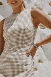Playsuit de estampado cuadros, fit ajustado, cuello barco, sin mangas, pinzas frontales, lazo amarrable posterior y cierre con cremallera oculta.