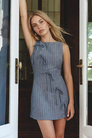 Playsuit de estampado rayas, fit ajustado, cuello barco, sin mangas, pinzas frontales, lazo amarrable posterior y cierre con cremallera oculta. Detalle frontal de lazos decorativos.