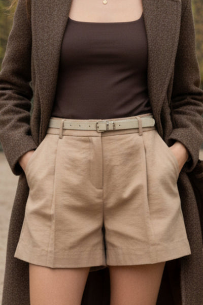 Short corto de fit recto, pinzas frontales, cintura alta con pretina y trabillas, bolsillos delanteros y vivos decorativos posteriores. Cierre frontal con broche y cremallera ocultos. Detalle de cinturón con hebilla en contraste.