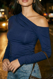 Top de fit ajustado, plisados en hombro, manga larga y cuello diagonal asimétrico con hombro descubierto.