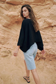 Blusa satinada tipo capa de fit fluido, manga larga amplia, cuello barco y bajo asimétrico.