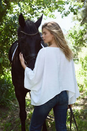 Blusa satinada tipo capa de fit fluido, manga larga amplia, cuello barco y bajo asimétrico.