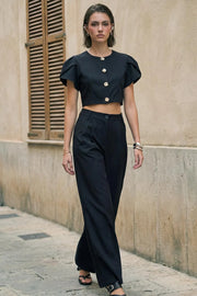 Blusa corta de fit recto, manga corta amplia con abertura, olanes y plisados en hombros, cortes frontales con pinzas, cuello redondo y cierre frontal con hilera de botones en contraste.