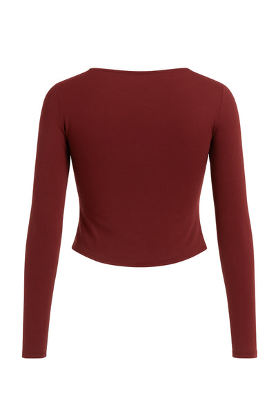 Top corto de fit ajustado, cuello barco, manga larga, botones decorativos en diagonal y bajo asimétrico frontal.