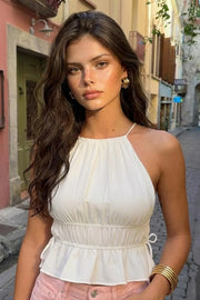 Top corto de cuello halter con plisados, tirantes delgados, detalle de rib con plisados y lazos laterales en costados, peplum con olanes en bajo y cierre posterior con botón y ojal.
