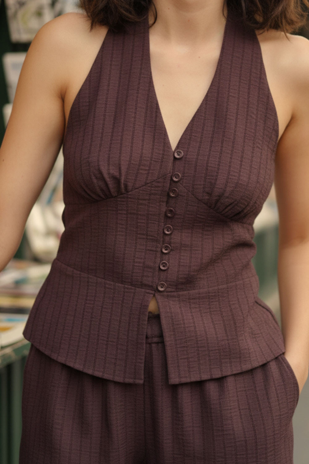 Top corto de estampado rayas, cuello halter con nudo amarrable posterior, escote v con cortes y plisados decorativos frontales, fit ajustado, escote en espalda con fruncido posterior, cierre frontal con hilera de botones y abertura en bajo.