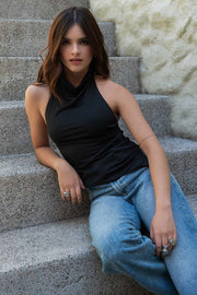 Top halter corto de fit ajustado, sin mangas, cuello halter fluido on plisados y escote en espalda. Detalle de bajo diagonal asimétrico.