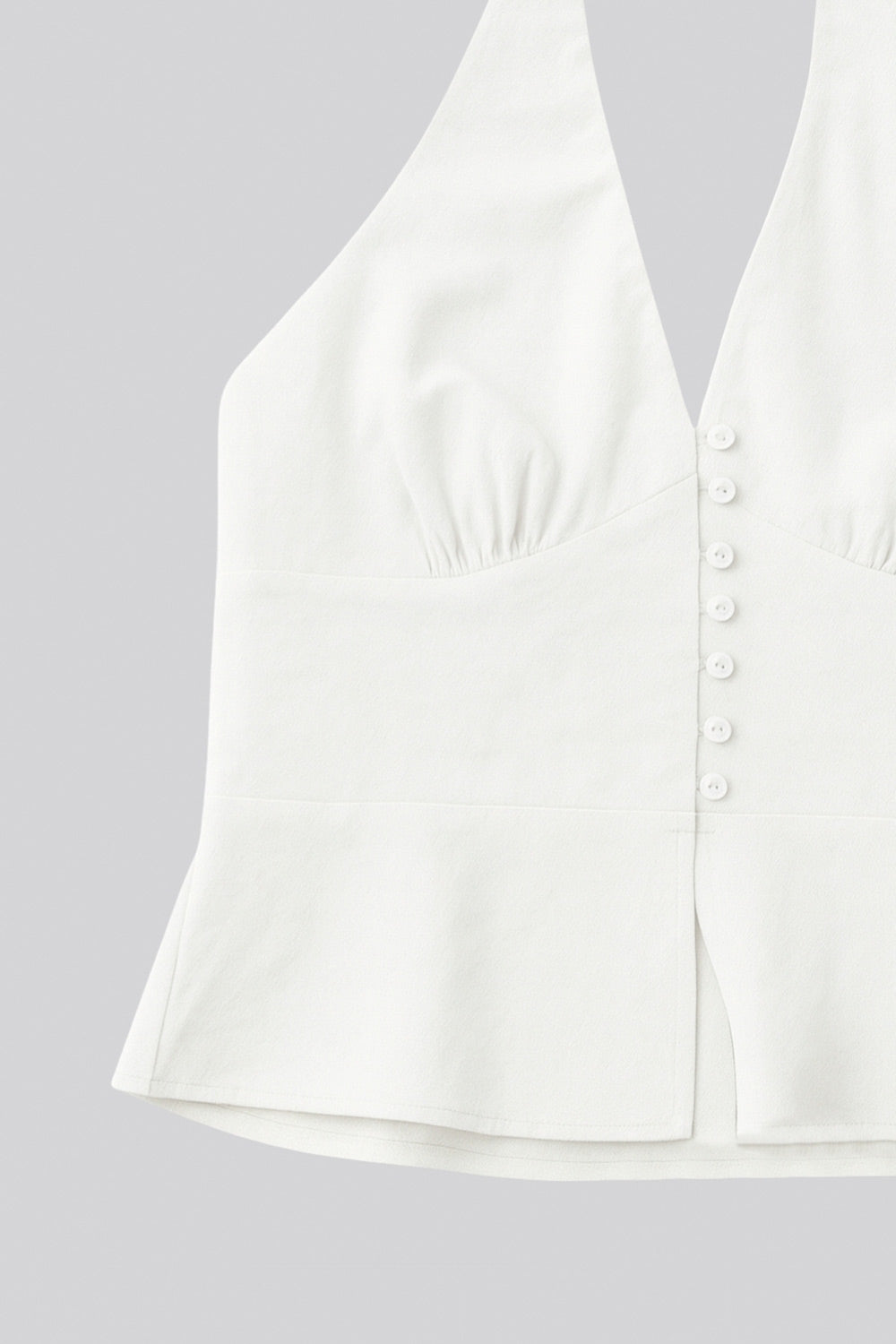 Top corto de cuello halter con nudo amarrable posterior, escote v con cortes y plisados decorativos frontales, fit ajustado, escote en espalda con fruncido posterior, cierre frontal con hilera de botones y abertura en bajo.