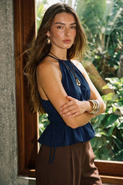 Top corto de cuello halter con plisados, tirantes delgados, detalle de rib con plisados y lazos laterales en costados, peplum con olanes en bajo y cierre posterior con botón y ojal.