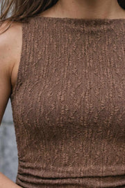 Vestido corto de cuello barco, sin mangas, plisados laterales en cintura, corte en a y detalle de textura en tejido.
