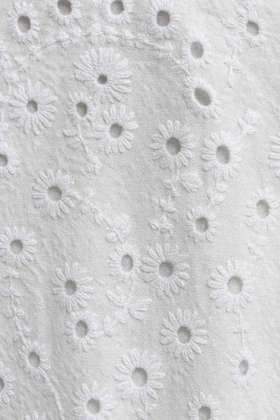 Vestido corto bordado de escote v con plisados frontales, corte en a, capas de olanes en bajo y tirantes con nudo amarrable. Cierre posterior con cremallera oculta y detalle de perforado en tejido.
