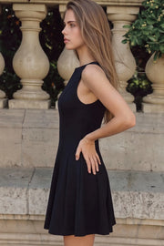 Vestido corto de cuello barco, sin mangas, cortes frontales, escote en espalda y corte en a con olanes en bajo.