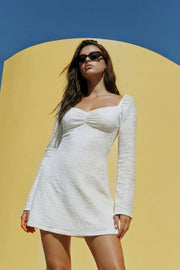 Vestido corto de escote corazón con cortes y plisados decorativos frontales, rib elástico en hombros, manga larga con puño amplio y corte en a. Detalle de textura en tejido y rib rizado en bajo.