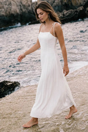 Vestido largo de fit ajustado, corte en a con olanes en bajo, tirantes delgados con nudo amarrable, escote recto y cierre posterior con cremallera oculta.