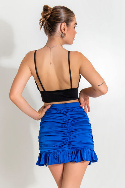 Falda corta satinada de fit ajustado, cintura alta con pretina elástica, fruncido frontal central y lateral. Bajo con olanes en borde y cierre lateral con cremallera oculta.