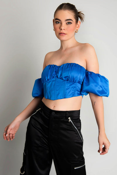 Top corset satinado de escote con detalles plisados, costuras frontales, bajo v frontal, hombros descubiertos y manga corta abullonada con olanes. Cierre con cremallera visible en contraste. 