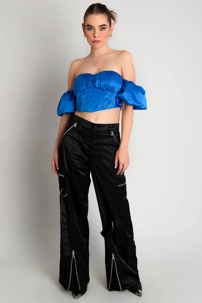 Top corset satinado de escote con detalles plisados, costuras frontales, bajo v frontal, hombros descubiertos y manga corta abullonada con olanes. Cierre con cremallera visible en contraste. 