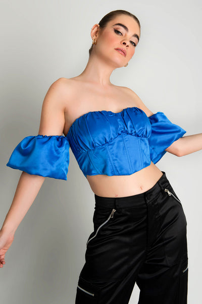 Top corset satinado de escote con detalles plisados, costuras frontales, bajo v frontal, hombros descubiertos y manga corta abullonada con olanes. Cierre con cremallera visible en contraste. 